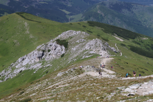 Gruppe von Menschen beim Wandern auf einem Berg mit grünem Gras und steinigem Gelände, Himmel im Hintergrund sichtbar