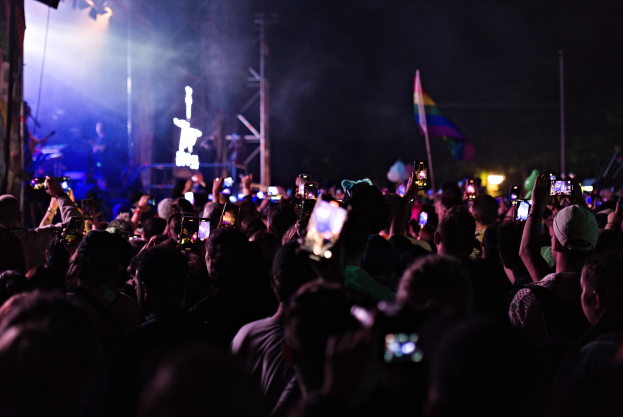 Eine Menge bei einem Konzert hält beleuchtete Handys hoch, während Menschen auf der Bühne Instrumente spielen.