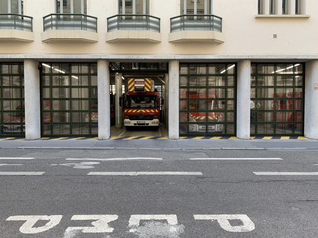 Feuerwache mit vor dem Gebäude geparktem Feuerwehrauto, mit Fenstern, Geländern, Säulen und Glastüren und einer Straße unten.