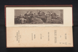 Ein altes Buch mit dem Titel "Die Geschichte der Jubiläums-Sänger" mit einem Schwarz-Weiß-Foto einer Gruppe von Menschen, einige sitzen, einige stehen, auf einer schwarzen Oberfläche.