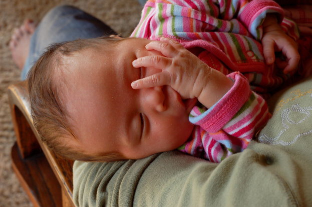 Eine Person, die ein schlafendes Kind hält und auf einem Matten sitzt.