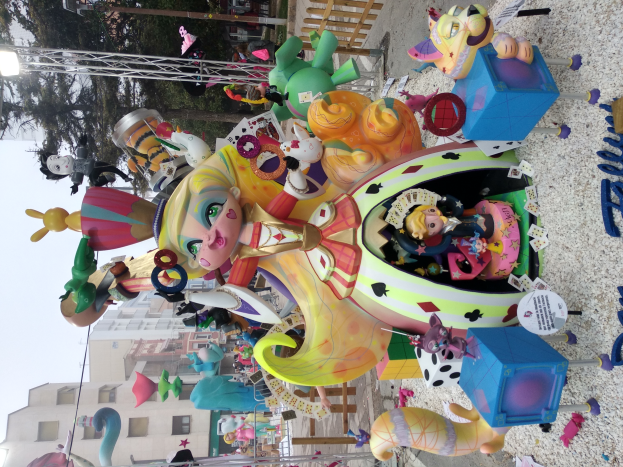 Eine Karussellfahrt ist in einer Stadtstraße aufgebaut, umgeben von Gebäuden, Bäumen und verschiedenen Gegenständen, mit Spielzeug ringsherum und dem Himmel darüber sichtbar.