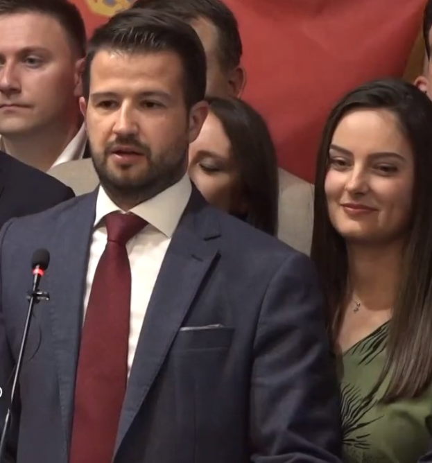 Ein Mann im Anzug spricht an einem Podium mit Mikrofon zu einer Menge hinter einem Banner, wahrscheinlich über ein Regierungssozialmedienverbot.