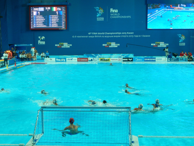 Gruppe von Athleten beim Wasserballspielen in einem Pool während der FINA-Weltmeisterschaften 2016 in Kazan, mit Zuschauern auf der linken Seite und einer beworbenen Wand im Hintergrund.