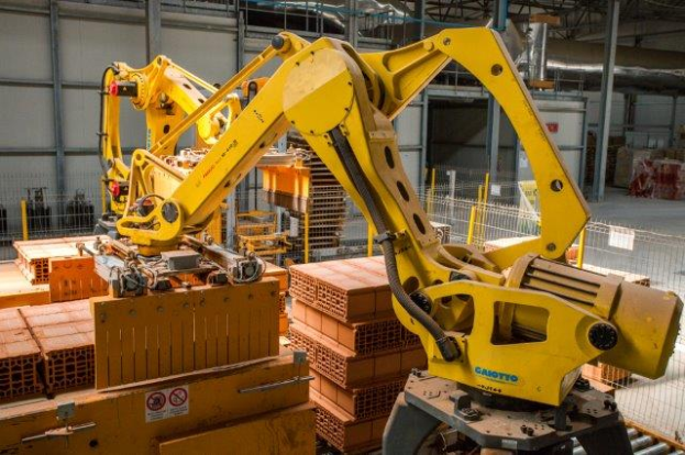 Ein großes Lager voller numerous boxes, Kräne, einen Zaun, Pfosten und andere industrielle Ausrüstung, mit einer Wand im Hintergrund, die eine größere industrielle Umgebung suggeriert.