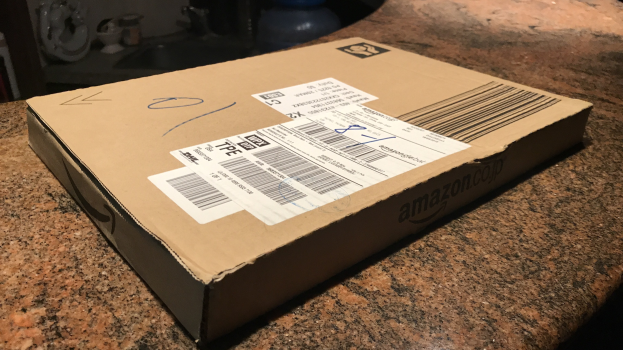 Kartonbox mit der Aufschrift 'Amazon Prime Day' auf einer Arbeitsplatte stehend mit einigen Gegenständen im Hintergrund.