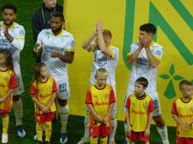 Eine Gruppe von Fußballspielern in Uniformen, die auf einem Ligue 1-Feld klatschen und einen Sieg feiern.