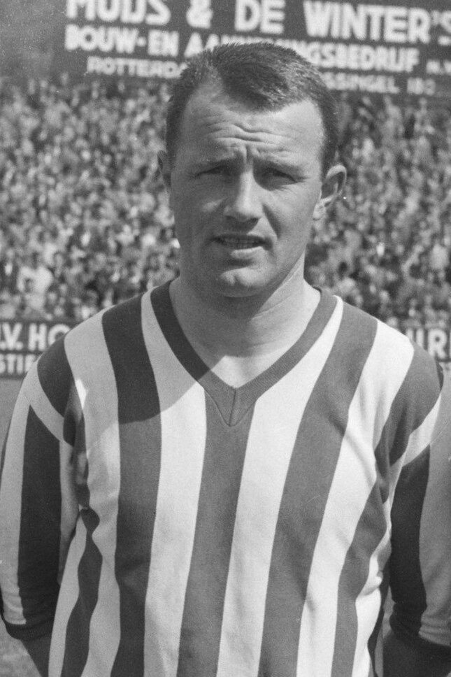 Schwarzes und weißes Foto eines Mannes in einem gestreiften Hemd, der vor einer Menge steht, mit einer Tafel im Hintergrund.