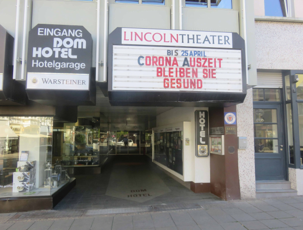 Außenansicht des Lincoln Theaters in Berlin, Deutschland, mit Glasfenstern und -türen sowie einer Tafel und einem belebten Stadtbild im Inneren.
