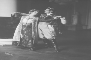 Ein Mann und eine Frau tanzen in einem Ballsaal, mit einer Säule und einer Wand im Hintergrund, auf einem alten Schwarz-Weiß-Foto.