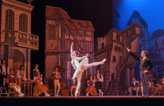 Zwei Tänzer performen auf der Bühne der Royal Opera House in London, mit einem Publikum im Hintergrund und einem Bildschirm mit Gebäudeabbildungen dahinter.