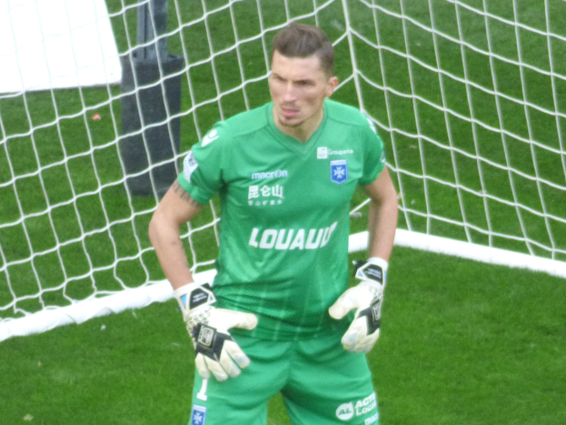 Ein Torwart in grüner Uniform steht vor einem Fußballtor auf saftig grünem Rasen, mit Handschuhen.