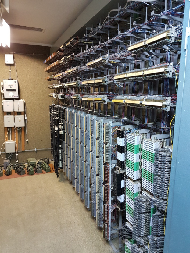 Großer Raum voller numerous wires und elektronische Geräte auf dem Boden, einschließlich Servern und Kabeln, was auf ein Rechenzentrum mit einer Wand auf der linken Seite hinweist.