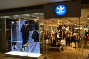 Ein Adidas-Laden in einem Einkaufszentrum mit Schaufensterpuppen, Kleidung, Schuhen und einem Schild mit dem Adidas-Logo, das auf einen Adidas Originals-Laden hinweist.