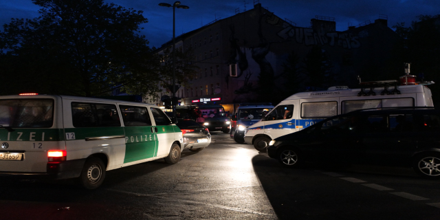 Eine Gruppe von Polizeiwagen, darunter ein Van, ein Auto und ein Rad, geparkt an der Seite einer Straße bei Nacht mit Gebäuden, Bäumen, Laternenpfählen und einem sternenklaren Himmel im Hintergrund.