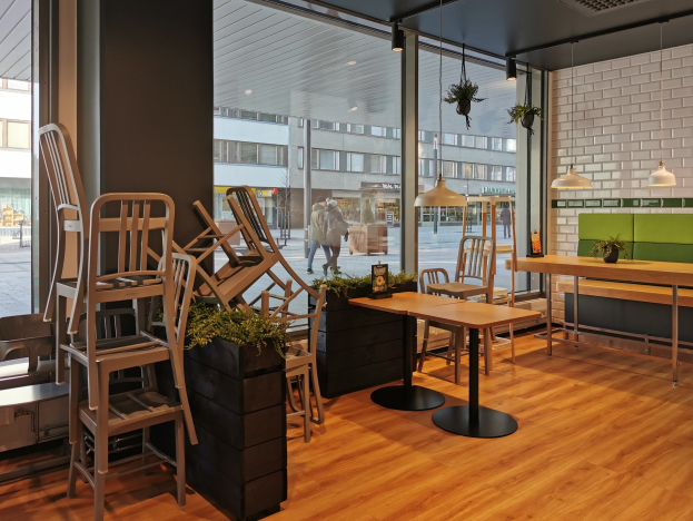 Ein Restaurant in Berlin mit Holztischen und -stühlen vor einem großen Fenster, das Fußgänger, Gebäude und Straßenelemente zeigt.
