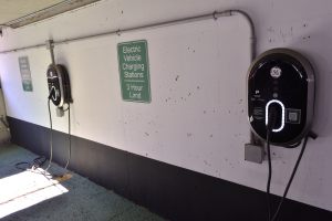 Ein Elektrofahrzeug-Ladestation in einer Tiefgarage mit zwei an der Wand angebrachten Ladesäulen und Tafeln mit Text darauf, der Boden ist unten im Bild zu sehen.