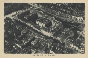 Schwarzes und weißes Luftbild einer dichten Stadtlandschaft mit einem zentralen Wolkenkratzer und Text unten.