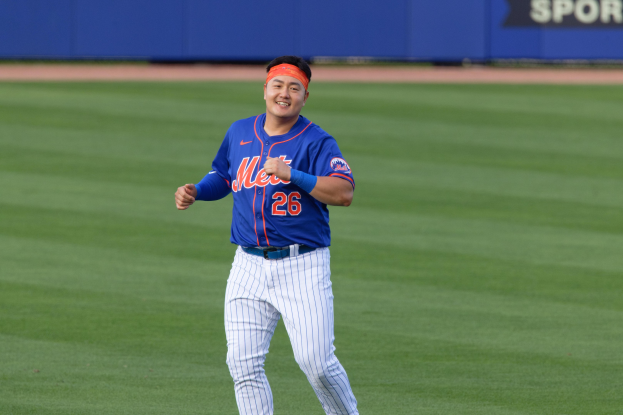 Baseballspieler in einem blauen T-Shirt, weißen Hosen und einem orangen Stirnband, der über ein Feld läuft und dabei strahlt, mit einem blauen Brett im Hintergrund.