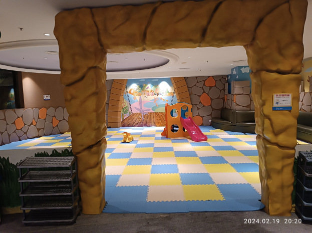 Kinderspielbereich mit einem zentralen Torbogen, verstreuten Spielzeugen, Regalen auf beiden Seiten, einer bemalten Wand im Hintergrund und Deckenbeleuchtung.