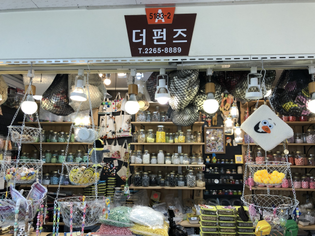Ein unordentlicher Laden in Seoul mit verschiedenen Artikeln wie Körbchen, Lichtern, Flaschen und Spielzeugen auf Regalen, mit einer Tafel öber der Tür, die ihn als einen der besten koreanischen Läden ausweist.
