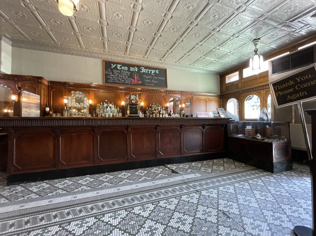 Großer Raum mit einer zentralen Bar, Deckenbeleuchtung, Flaschen auf einem Tisch und einer Schiefertafel auf der rechten Seite, Located in the Tom and Jerry Pub in London.