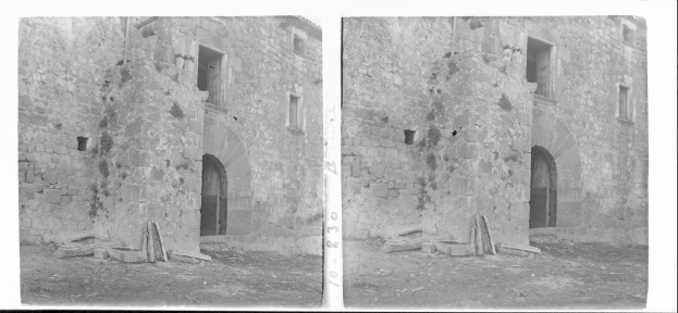 Schwarz-weiß-Foto von alten Steinschlossruinen mit intakten Wänden und Fenstern, umgeben von verstreuten Steinen und hölzernen Gegenständen.