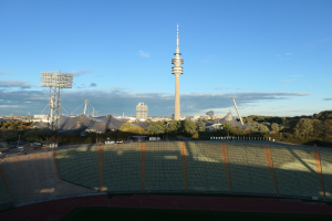 Olympiastadion in Berlin, Deutschland, mit dem Fernsehturm TV-Turm im Hintergrund, umgeben von Bäumen, Gebäuden und Lichtern unter einem bewölkten Himmel.