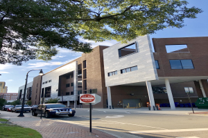 Ein großes mehrstöckiges Gebäude mit zahlreichen Fenstern, umgeben von Straßenlaternen, Fahrzeugen, Schildern, Bäumen und einem bewölkten Himmel, als das neue Studentenwohnheim der University of Washington identifiziert.