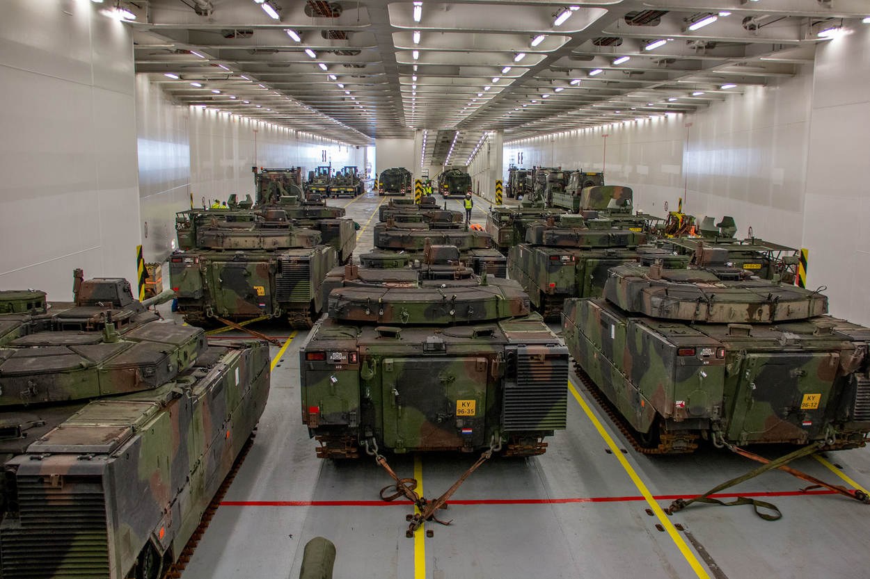 Ein grosser Militaraerraum mit Reihen von Militaraerpanzer, beleuchtet von Deckenlichtern und umgeben von Waenden.