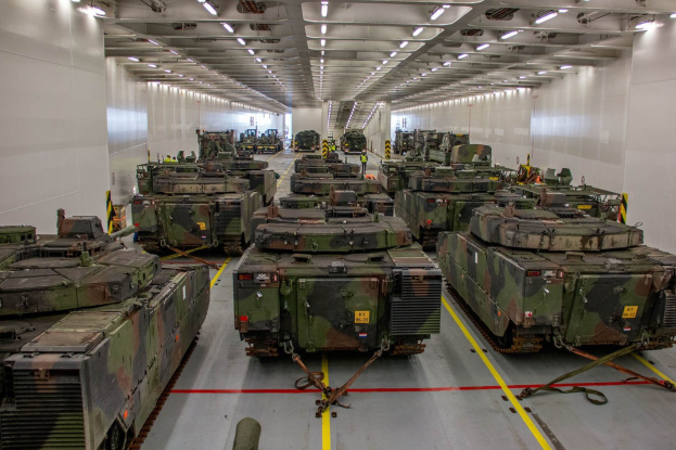 Ein grosser Militaraerraum mit Reihen von Militaraerpanzer, beleuchtet von Deckenlichtern und umgeben von Waenden.