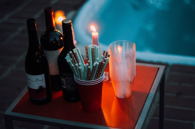 Ein Tisch am Swimmingpool mit zwei Weinflaschen, einer Kerze, Gläsern und Strohhalmen, was auf einen Abend am Pool hinweist.