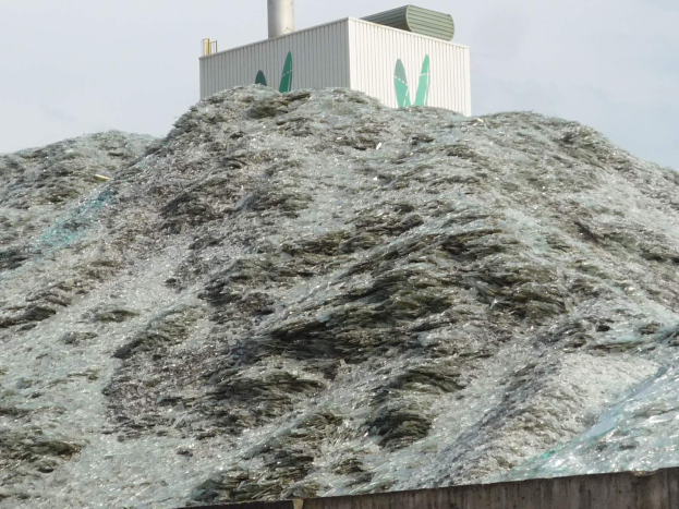 Großer Haufen aus Plastikabfall auf einer Zementwand mit einem Gebäude und einem klaren blauen Himmel im Hintergrund.
