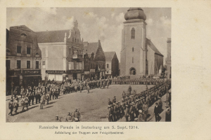 Ein Schwarz-Weiß-Foto eines Umzugs in Insterburg am 5. September 1914 mit vielen Menschen, Gebäuden und bewölktem Himmel sowie einem Text unten.