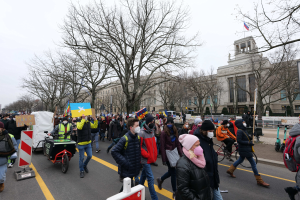 Eine große Gruppe von Menschen nimmt an einer Protestdemo in Washington, D.C. am 21. Januar 2020 teil und geht eine Straße entlang, wobei sie Schilder und Banner schwenken und einige Fahrräder fahren, mit Schildern, Bäumen und einem klaren blauen Himmel im Hintergrund.
