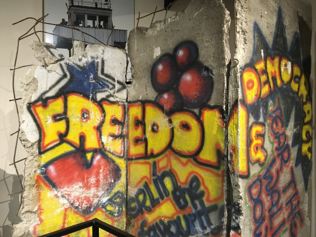 Eine Wand mit Graffiti, das "Freiheit und Demokratie" in fetten schwarzen Buchstaben liest, ein Geländer unten und ein Gebäude mit Fenstern im Hintergrund.