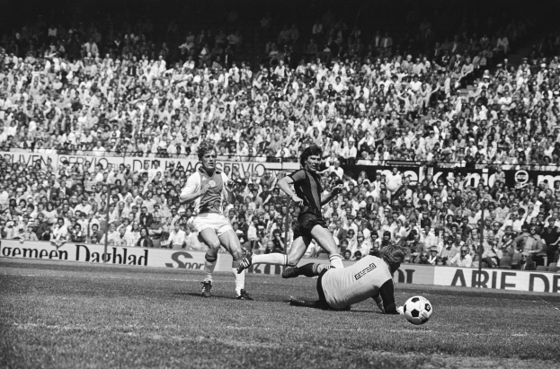 Schwarz-weißes Foto von Männern, die auf einem Feld Fussball spielen, mit Zuschauern im Hintergrund und einer Tafel mit der Aufschrift "Bundesliga 1978-79 Ajax 1-1 Hannover 96".