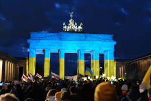 Menschenmenge mit Fahnen und Plakaten vor dem Brandenburger Tor, mit einer Fahne auf der rechten Seite des Bildes.