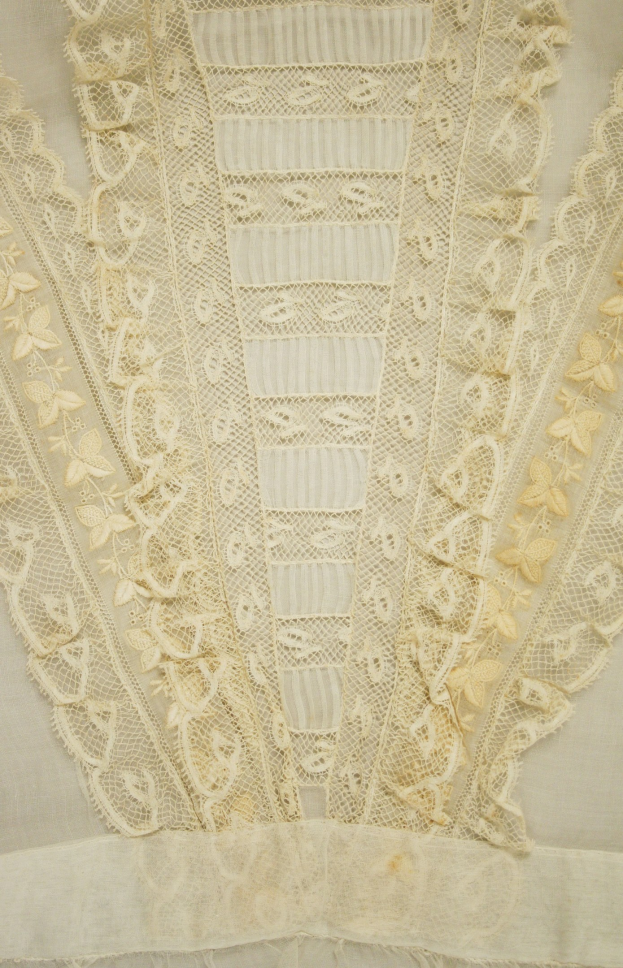 Nahaufnahme eines weißen Kleides mit feiner Spitze und detaillierten Mustern, das für den Sommer geeignet ist.