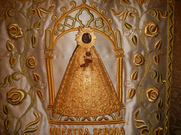 Goldbrokate Chasuble mit einer serenen Frau in einem hochgeschlossenen, langärmligen Kleid mit einem Dutt, umgeben von detaillierten Designs, Text und goldenen Bordüren.