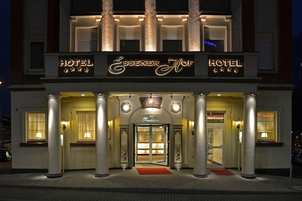 Das Essenerhof Hotel in Berlin, Deutschland, ein mehrstöckiges Gebäude mit Fenstern, Türen und Säulen, hat ein Namensschild und liegt entlang einer Straße mit Fahrzeugen rechts daneben, unter einem sichtbaren Himmel.