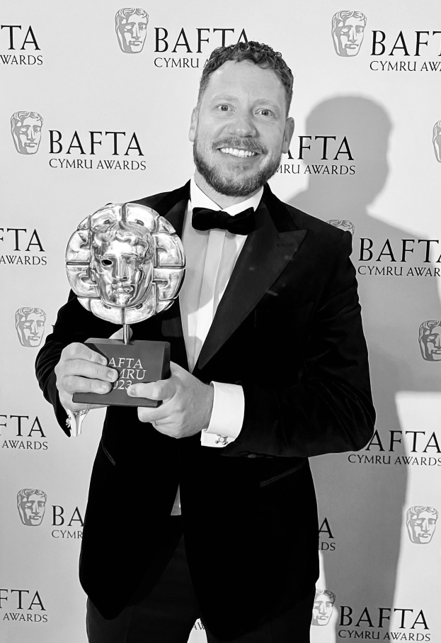 Ein Mann in einem Smoking, der eine BAFTA-Auszeichnung hält und lächelt, mit einem Hintergrundplakat, auf dem "BAFTA Awards 2018" steht