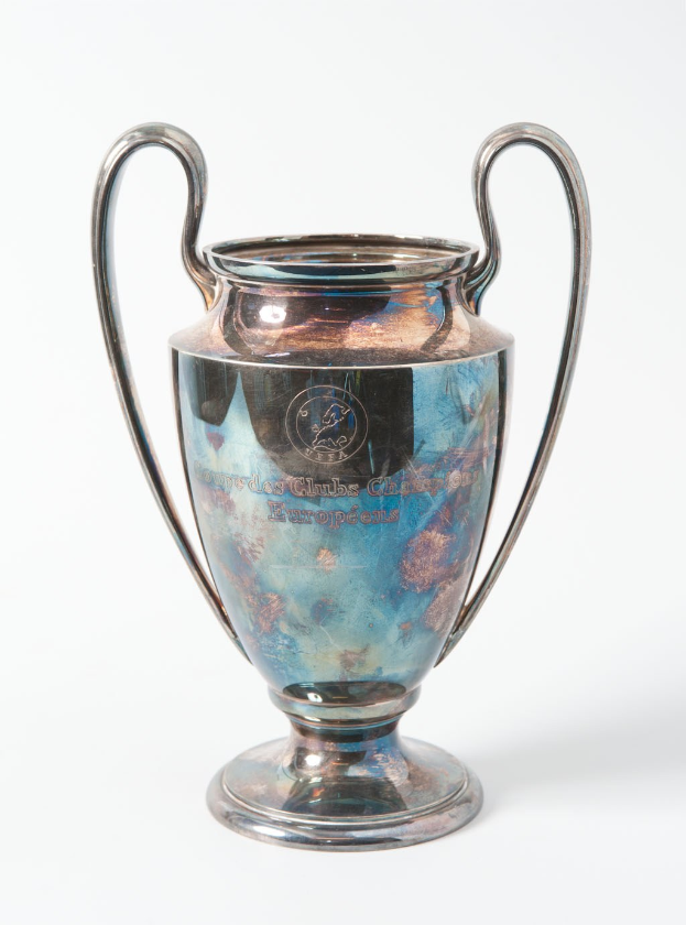 Der UEFA-Champions-League-Pokal, ein stahlerner Becher mit zwei Griffen, blau und silbern, mit der Inschrift "UEFA Champions League", vor einem weißen Hintergrund dargestellt.