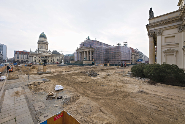 Großbaustelle mit Berliner Dom im Hintergrund, Bäumen auf der rechten Seite, Fahrzeugen auf der linken Seite und Himmel darüber.