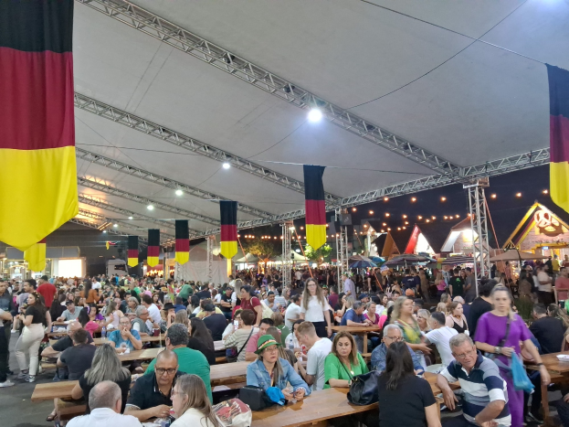 Eine große Gruppe von Menschen an Tischen unter einem Zelt auf dem Oktoberfest in München, Deutschland, mit Taschen und Gegenständen auf den Tischen und festlicher Dekoration im Hintergrund.