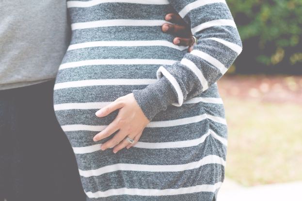 Schwangeres Paar im Freien mit Händen auf dem Bauch, tragend, umgeben von Bäumen.