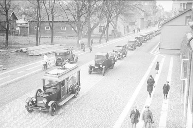 Ein Schwarz-Weiß-Foto einer Berliner Straße aus den 1930er bis 1940er Jahren mit Autos, Fußgängern, Gebäuden, Bäumen und einem klaren Himmel; Text unten lautet "1930er bis 1940er Jahre deutsche Autos in Berlin".