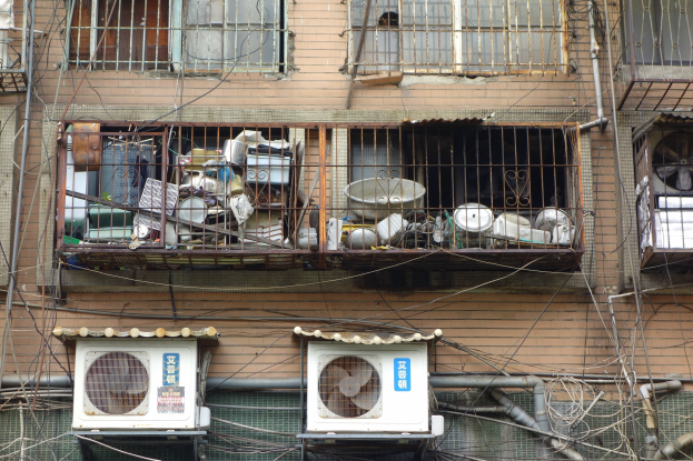 Ein Wohnhaus mit Fenstern, Eisengittern, Klimaanlagen, Rohren und Käblein an der Seite.