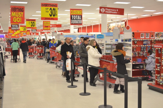 Ein volles Walmart-Regal während des Black Friday-Verkaufs, mit Einkaufswagen schiebenden Kunden, Taschen haltenden Kunden und Waren durchsuchenden Kunden unter Deckenlampen und nahe von bunt dekorierten Pfosten.