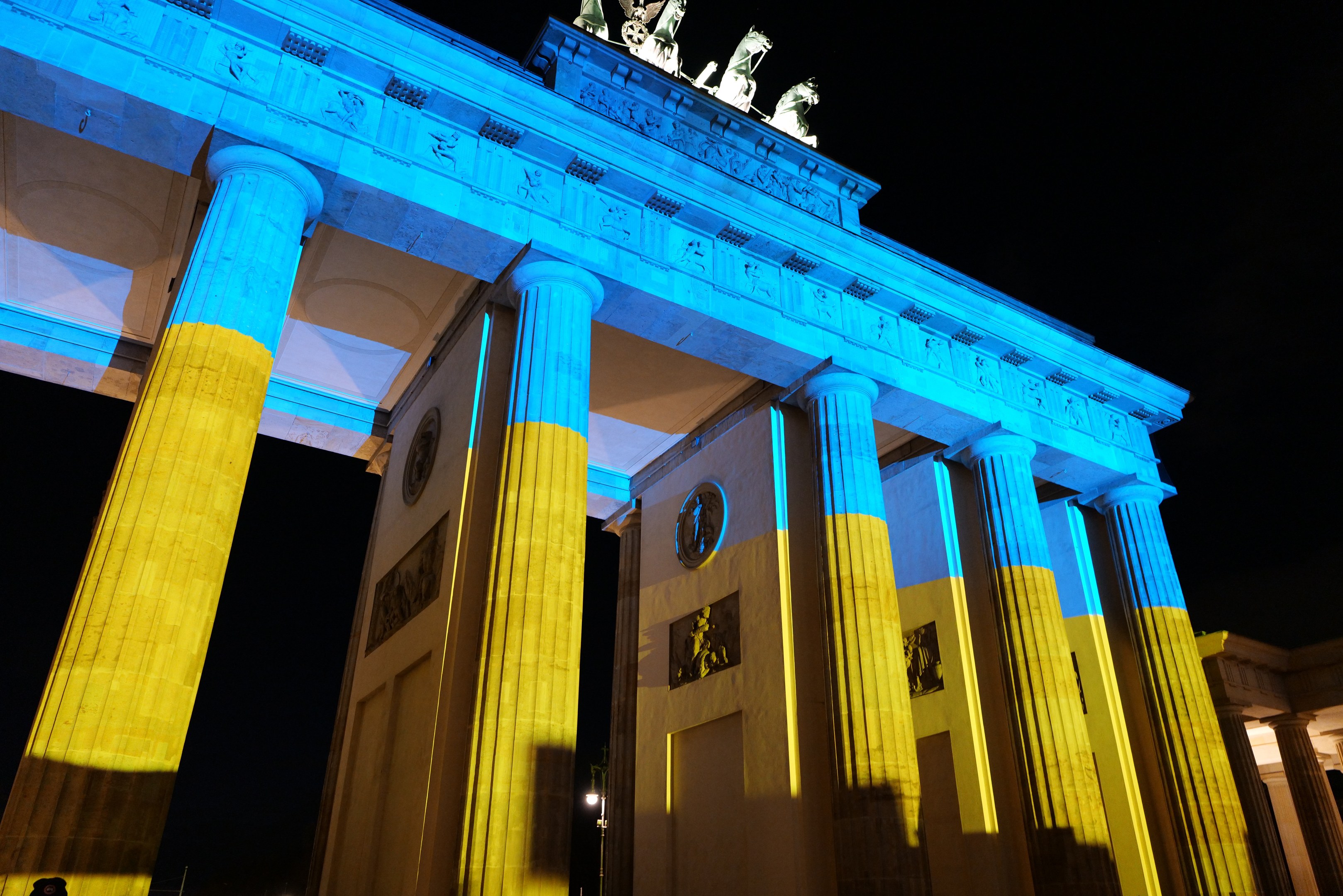 Das Brandenburger Tor in Berlin, Deutschland, erstrahlt in Blau und Gelb und präsentiert sich mit seinen Skulpturen gegen einen dunklen Hintergrund.